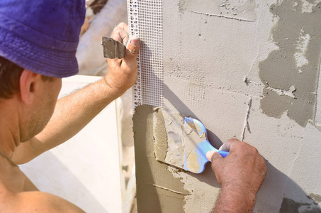 五十岁的手工工人用墙抹灰工具翻新房子。泥水匠用刮刀和石膏翻新墙壁和角落。壁泥安装。建筑整理工程