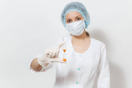 年轻的医生妇女与口罩, 无菌帽, 手套在白色背景隔离。女外科医生在医疗礼服举行沙漏。医护人员, 医学理念。时间不多了