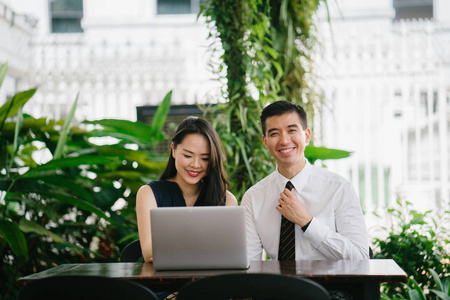 两个微笑的商业人士 律师, 顾问等 的肖像或夫妇微笑的中间讨论一台笔记本电脑在办公室与绿色的背景。他们专注于笔记本电脑