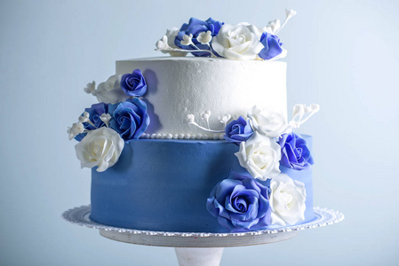 美丽的两个分层的白色和蓝色婚礼蛋糕装饰花糖玫瑰。优雅假日甜点概念