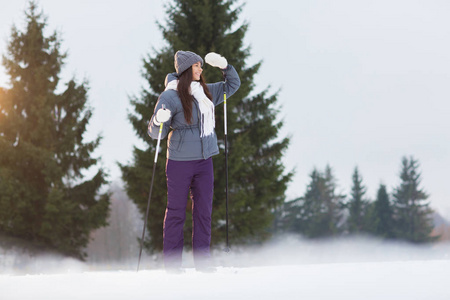 滑雪的年轻女子看着远处, 而在冬季森林或公园的休闲消费