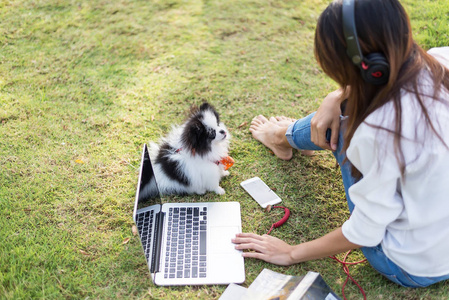 妇女坐在绿草使用 labtop。女孩喜欢听音乐和阅读一本书, 在公园的草地上玩笔记本电脑早晨