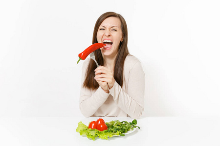 有趣的女人在餐桌上用树叶沙拉生菜, 西红柿在盘子上, 胡椒粉在叉子上隔绝在白色的背景上。适当的营养, 素食, 健康的生活方式节食
