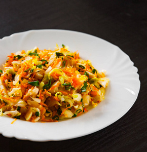 新鲜蔬菜沙拉配卷心菜和胡萝卜在黑木桌上的白色盘子里