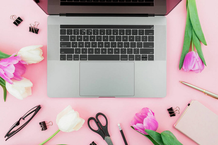 办公桌与笔记本电脑, 白色郁金香, 眼镜, 钢笔和剪刀在粉红色的背景。平躺。顶部视图。复制空间的自由职业者组合