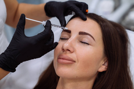 在面部美容注射过程中, 用注射器把美丽的女性脸部和 cosmetologists 手闭上。复兴和 hydratation。美容理