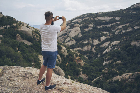 男徒步旅行者正在山顶上用智能手机拍照。
