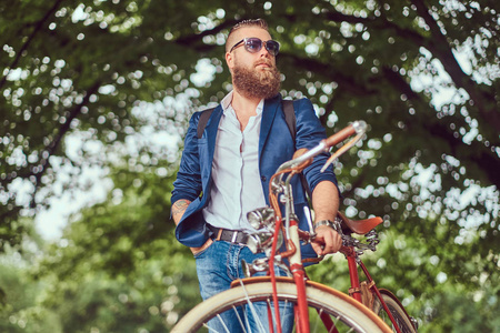 旅行者穿着休闲衣服和戴着太阳镜的背包, 在骑着复古自行车的城市公园里放松身心。