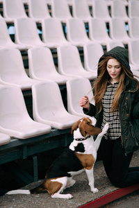 年轻的时髦女孩与她的宠物爱沙尼亚猎犬狗玩，俊平和拥抱和室外在玩老体育场