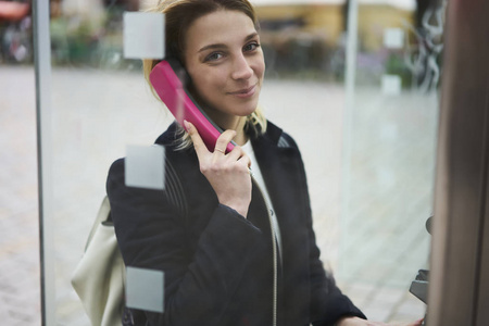 有吸引力的金发女性旅行者的肖像在电话亭外面的电话交谈谈论旅行冒险, 年轻的时髦女孩在周末旅行期间拨打国际电话