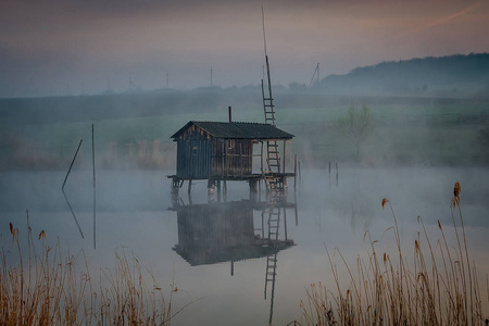 清晨雾中的水面上的钓鱼屋