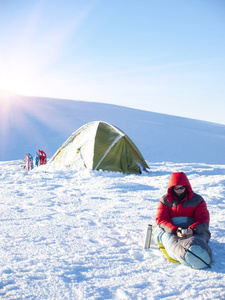 一个男人坐在睡袋里附近的帐篷和雪