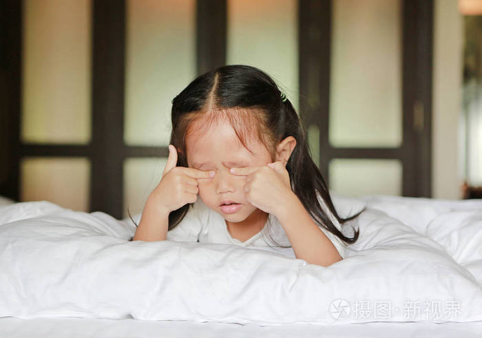 可爱的小亚洲女孩躺在床上揉眼睛