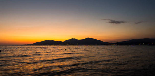 日落在靠近海边的小城市上空。红色和橙色颜色与水海在前景。浪漫风光