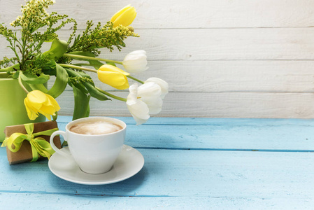 咖啡杯, 黄色和白色的郁金香花在一个绿色的花瓶和一个小礼物在绿松石木材, 白色木质背景与复制空间