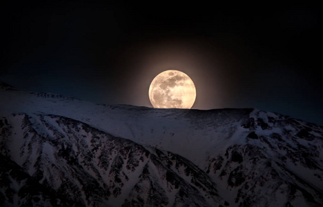 超级大月亮升起在黄昏的时候，白雪皑皑的高山。在晚上关门的视图升起的月亮