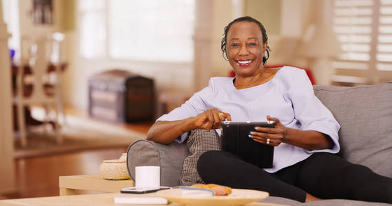 一位黑人老年妇女一边看着相机, 一边高兴地使用平板电脑