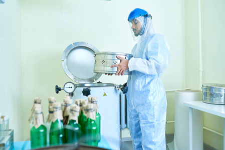 年轻科学家的侧面画像穿着防护套装将有害物质的试管放入医用实验室加工机中
