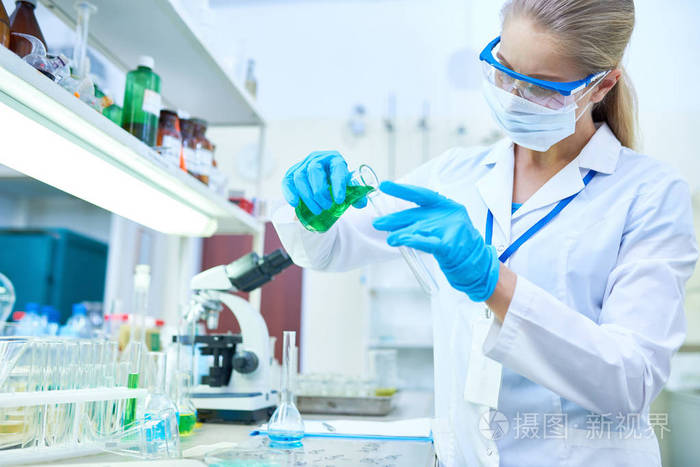 戴防护手套的女科学家肖像在医学实验室研究化学药品时, 将有色液体