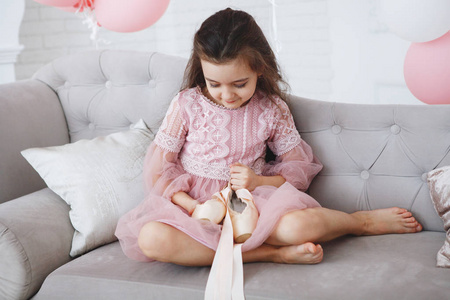一个穿着粉红色连衣裙的年轻芭蕾舞演员坐在灰色的沙发上, 手里拿着指出。