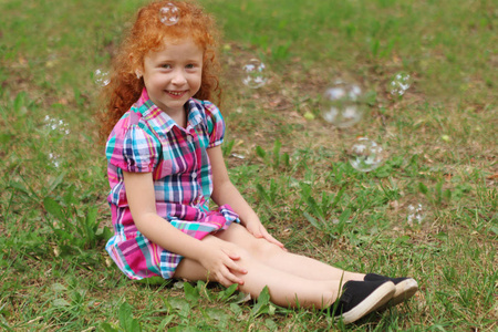 红头发的小女孩坐在草丛之中，气泡在夏天