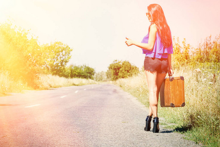 黑发美女旅行者带着手提箱上路, 搭便车。旅行的概念, 冒险, 假期, 自由。等待汽车或公共汽车