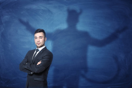 商人站立时整个手和他的影子在他身后的蓝色黑板上尾巴像魔鬼
