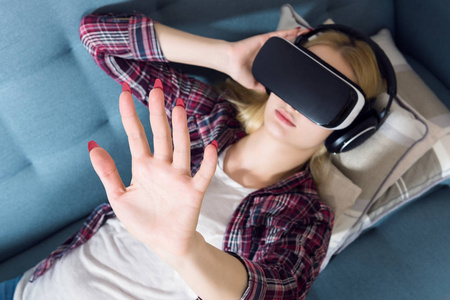 有魅力的女人穿上虚拟现实的护目镜，躺在沙发上。虚拟现实耳机。生活方式虚拟现实的概念