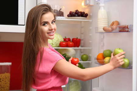 漂亮的女孩在冰箱里选择蔬菜。健康食品概念