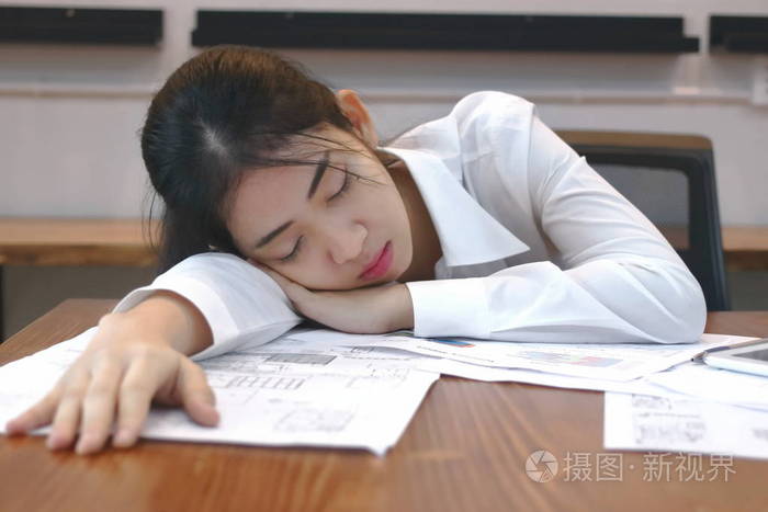 疲惫的劳累过度的年轻的亚洲商人躺在办公桌上的办公室