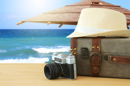 旅行者古董行李, 照相机和软呢帽帽子在木桌前面在海风景。假日和假期概念
