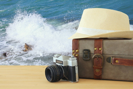 旅行者古董行李, 照相机和软呢帽帽子在木桌前面在海风景。假日和假期概念