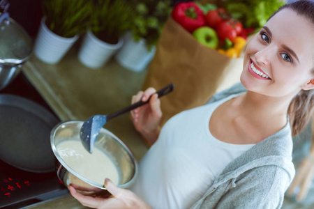 年轻女人准备站在桌子旁边的时候厨房里的薄煎饼。在厨房里的女人。在厨房做饭