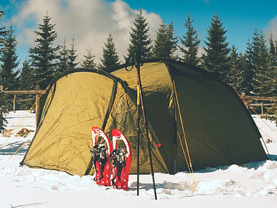 冬天露营在雪在森林里。树间隐藏的绿色帐篷