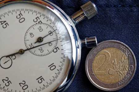 欧元硬币与面额2欧元和秒表在过时的蓝色牛仔布背景商业背景