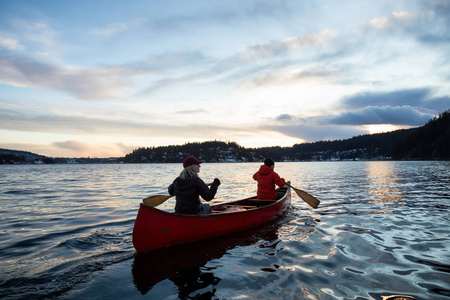 一对夫妇的朋友在一个木独木舟是在一个充满活力的日落在加拿大山脉包围的入口划。印度的手臂, 靠近深湾, 温哥华, 不列颠哥伦比亚省
