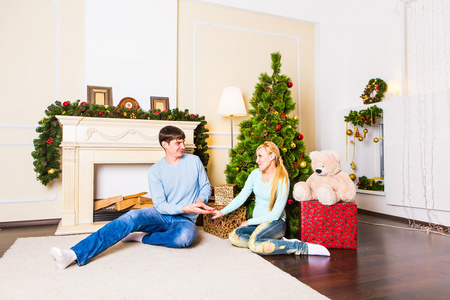 好爱的情侣坐在壁炉前的地毯上。女人和男人庆祝圣诞节
