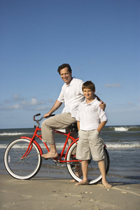 父亲骑自行车，儿子在沙滩上。