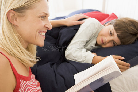 女人对着床上的小男孩微笑着看书