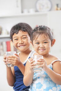 两个小女孩和男孩每人拿着一杯牛奶