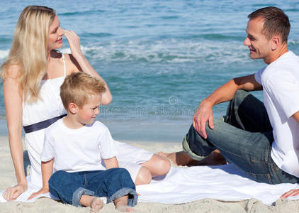 带着儿子坐在沙滩上微笑的父母