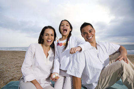 在海滩上坐在毯子上的西班牙裔家庭