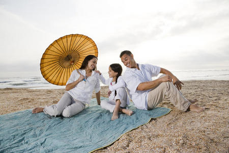 带着小女孩躺在沙滩毯上的西班牙裔家庭