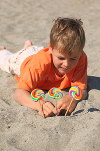 高加索男孩躺在沙滩上，棒棒糖成了沙子