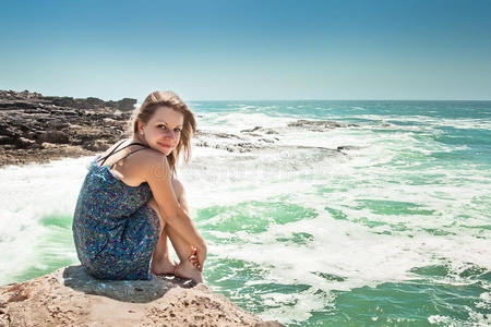 穿着衣服坐在海上岩石上的女孩
