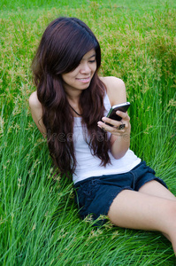 亚洲可爱女孩在草地上发短信