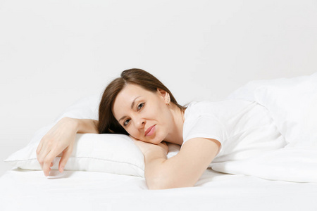 平静的年轻的黑发妇女躺在床上, 白色的床单, 枕头, 毯子在白色的背景。微笑的美女女性在房间里消磨时间。休息, 放松, 心情好的