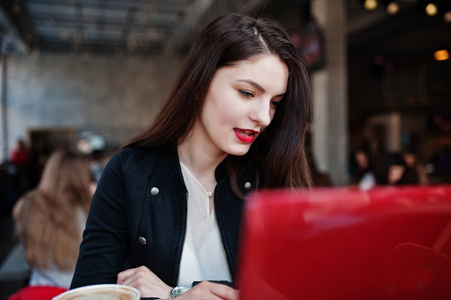 黑发女孩坐在咖啡馆和工作与红色笔记本电脑