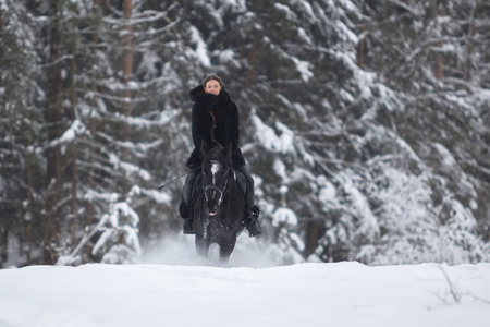 一个女孩骑着黑马穿过雪地在冬天的森林背景下, 前视图