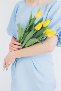 穿蓝色连衣裙的女孩捧着一束黄色的郁金香。